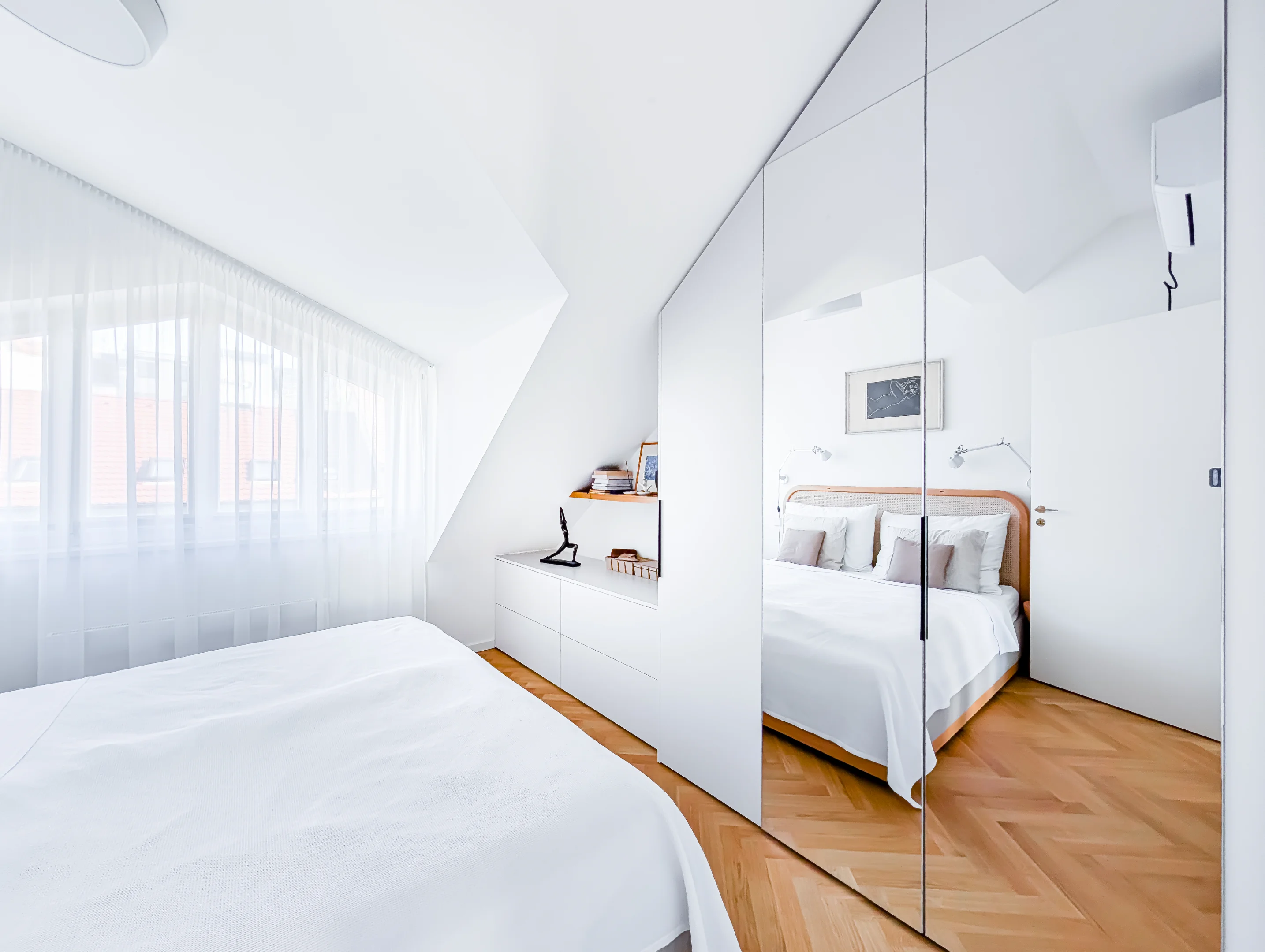 Světlá ložnice s postelí zrcadlovou skříní a dřevěnou podlahou